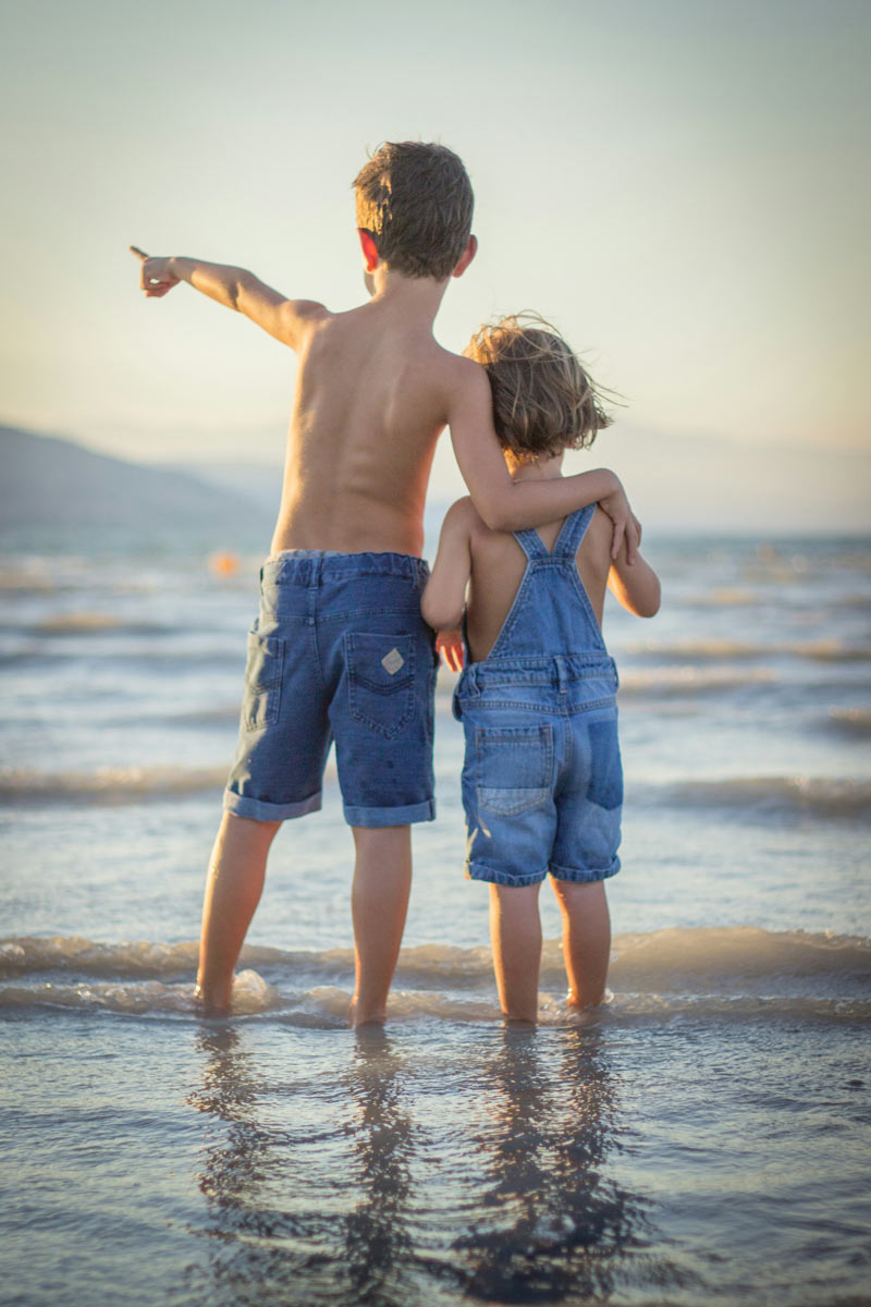 a big brother points to something in the ocean to show his little brother