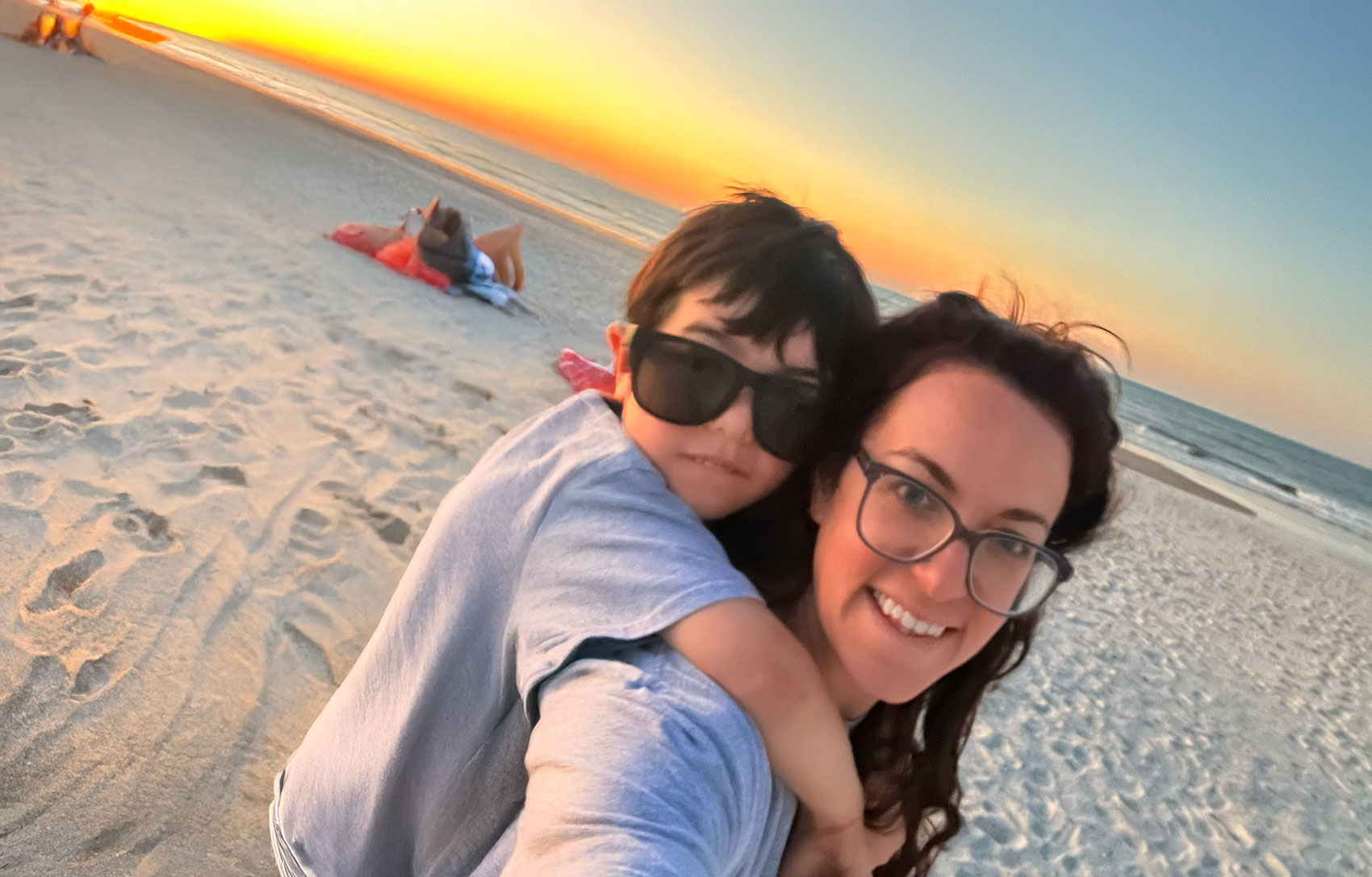 sunset_mom_son A smiling mother carries a little boy on her back as they walk down the beach at sunset